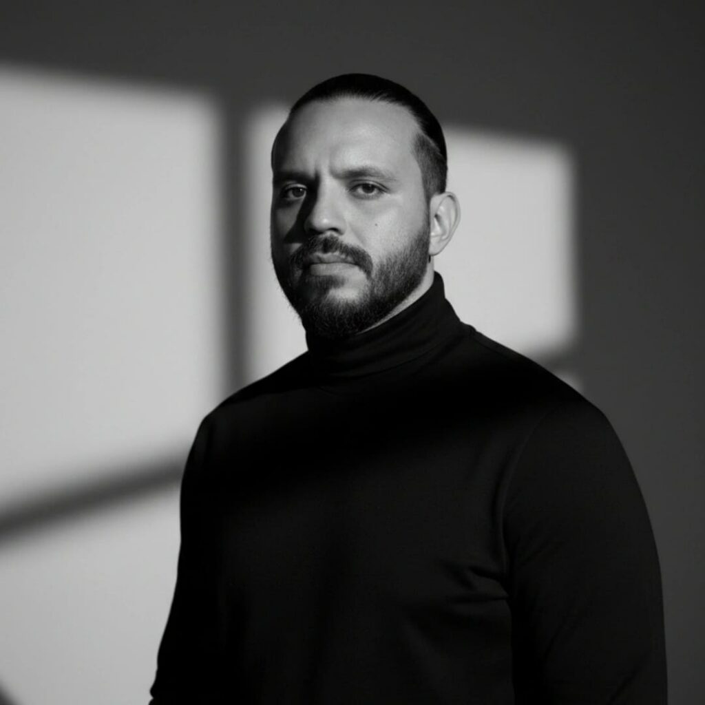 Portrait artistique en noir et blanc de Mohammed Amine Laarej, connu sous le nom d'artiste A-MIN. Il porte un col roulé noir, avec un jeu d'ombres géométriques projetées sur un fond clair, créant une atmosphère mystérieuse et cinématique.